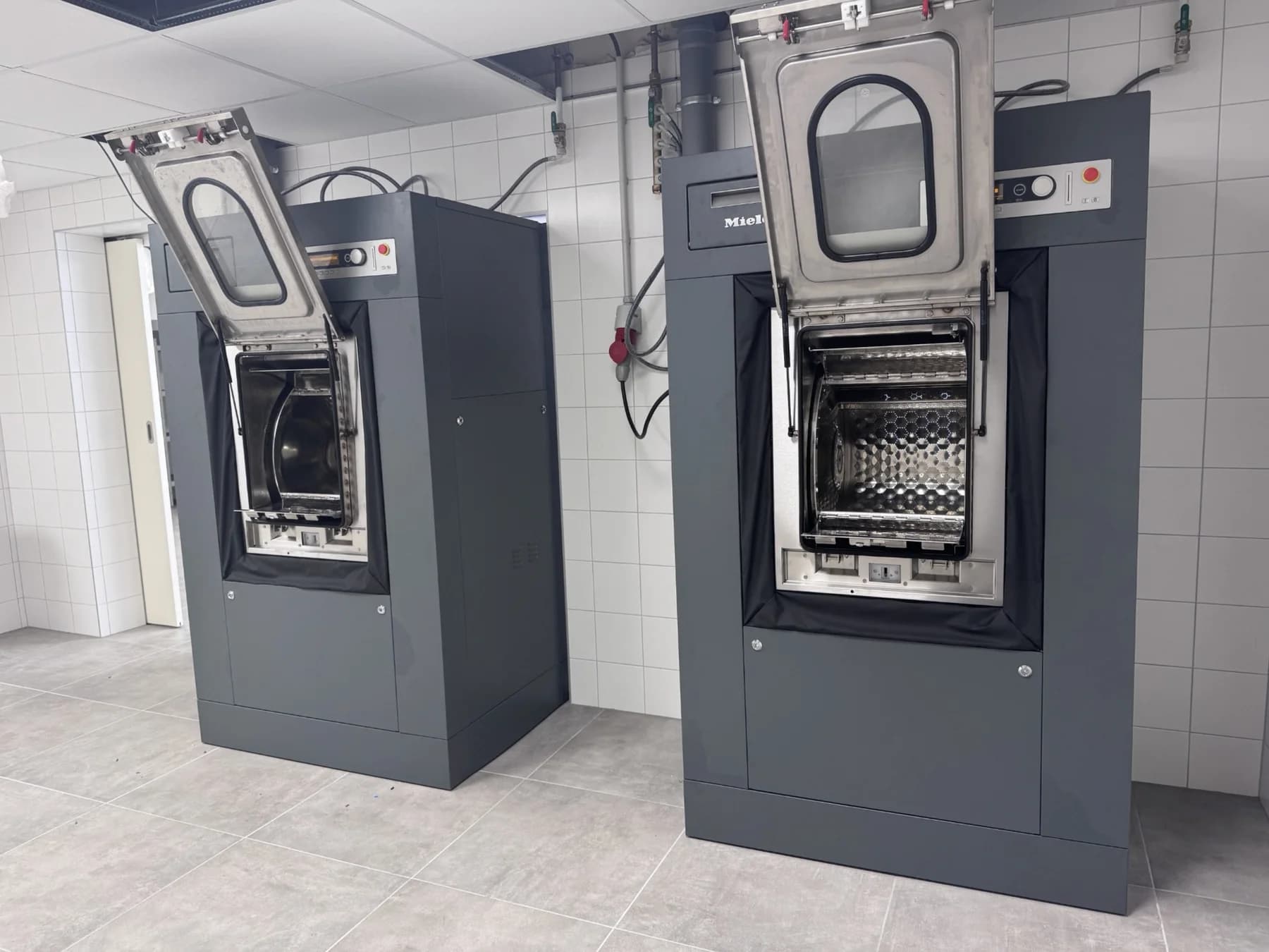 Deux lave-linge barrières Miele Professional, portes ouvertes, dans une blanchisserie hospitalière