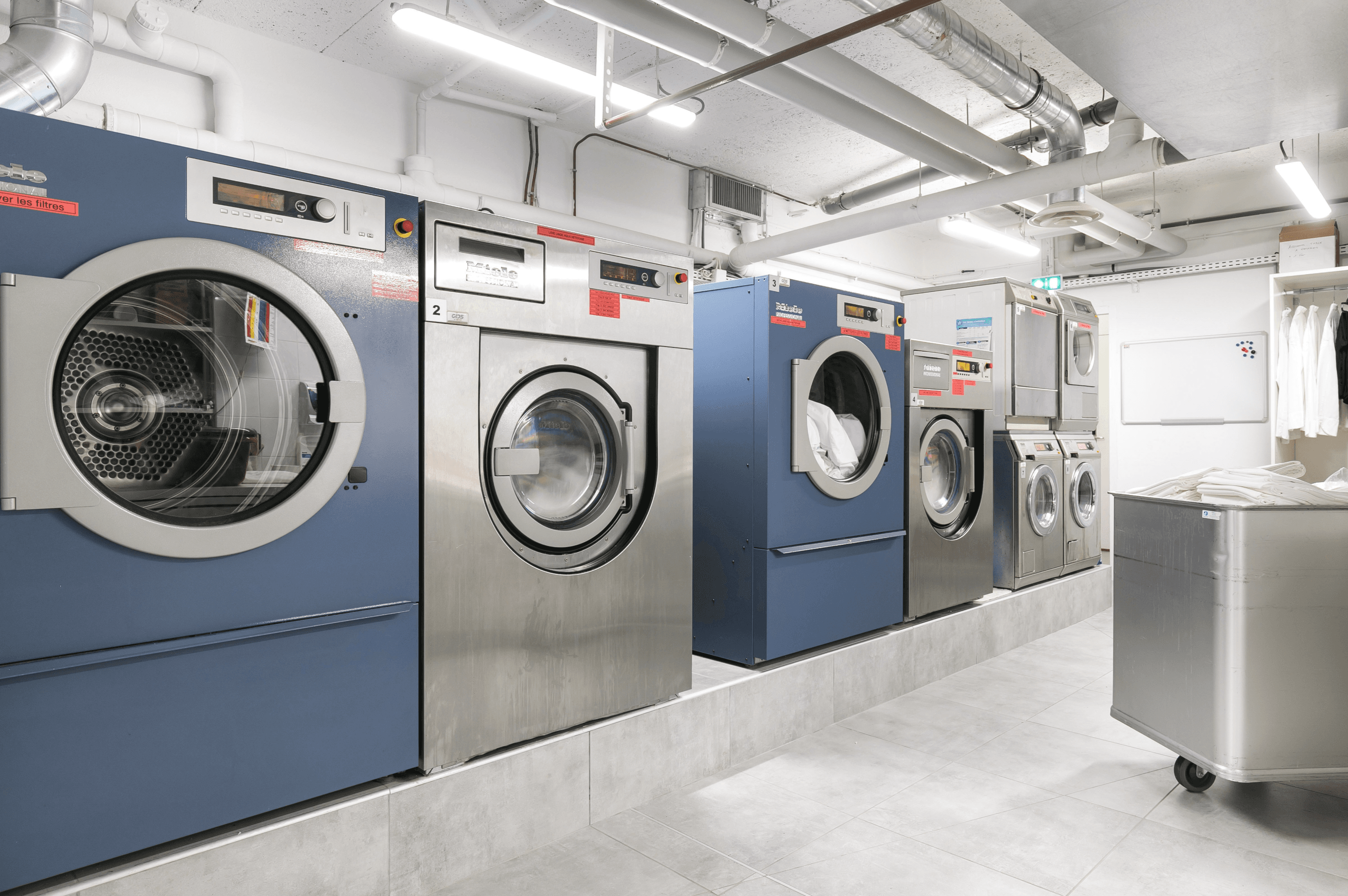 Lave-linge et sèche-linge Miele Professional dans une buanderie avec chariot de linge