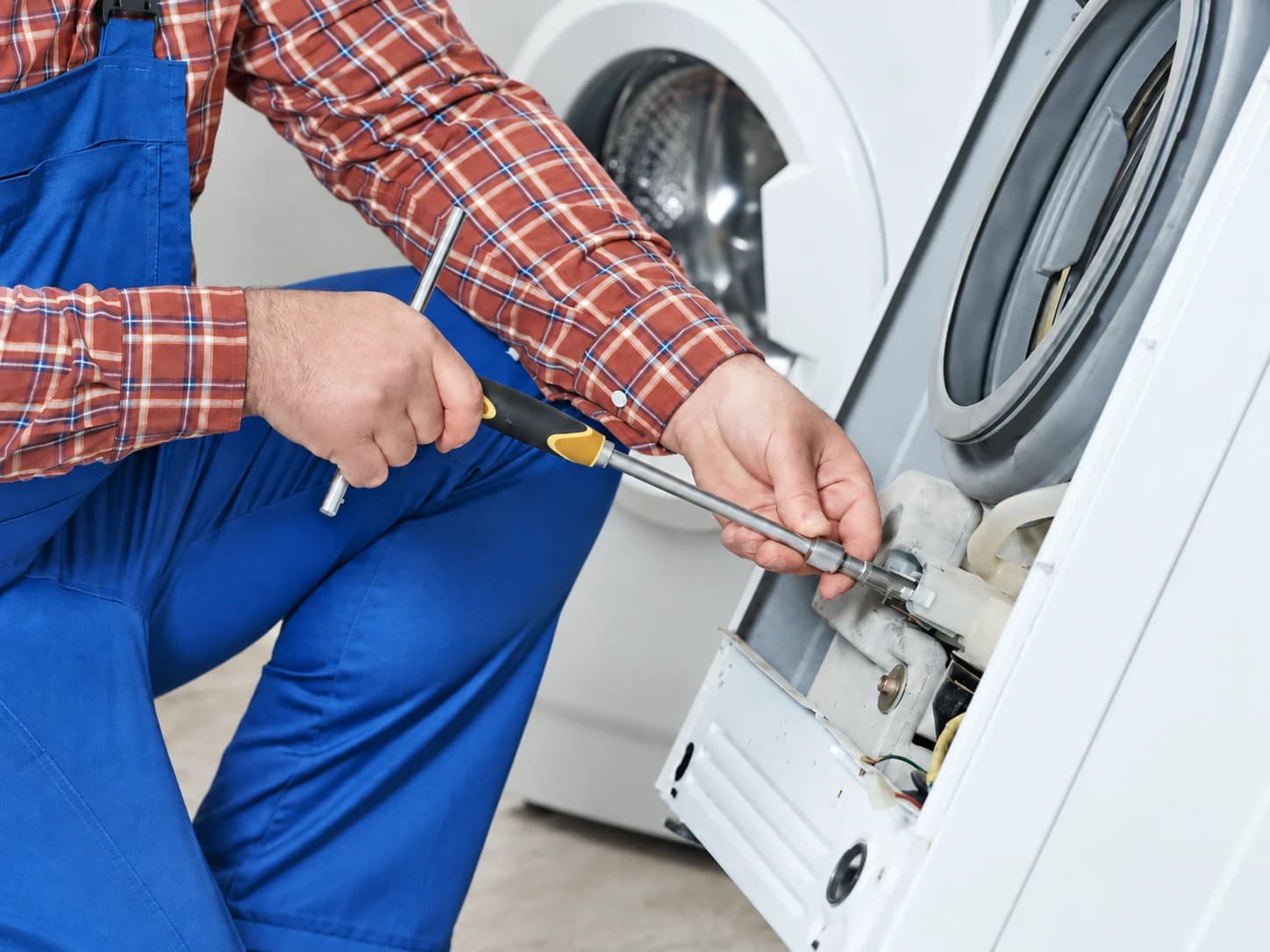 Technicien intervenant sur une fixation derrière la façade ouverte d’un lave-linge